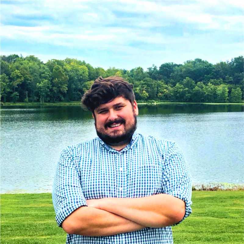 An image of Quentin smiling in front of a lake on a nice day